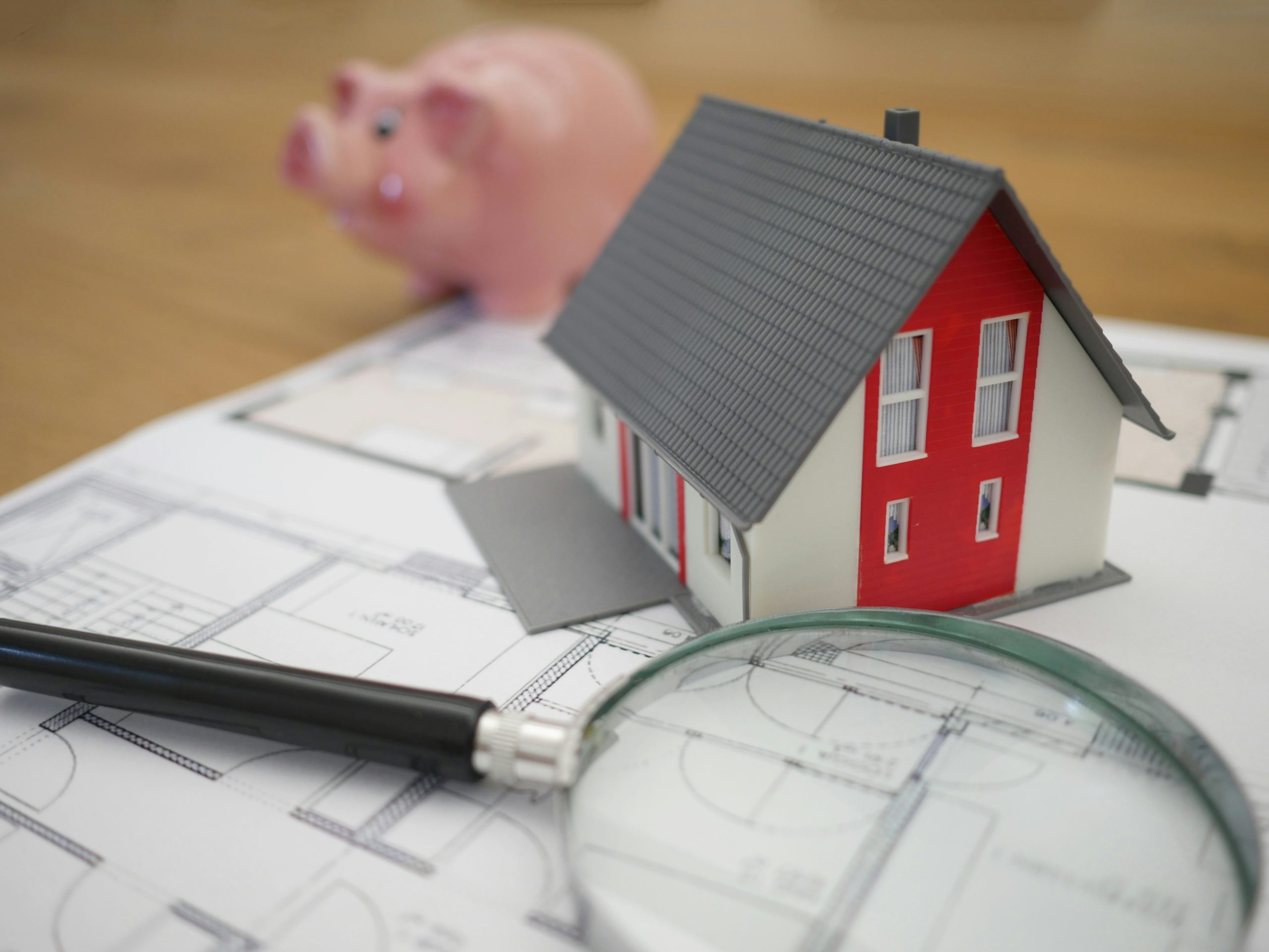 miniature house, blueprint, magnifying glass, and piggy bank on a table